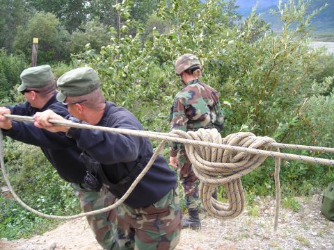 2003 Jeep TJ - Three individuals in camouflage uniforms are engaged in an activity involving ropes and pulleys in an outdoor, wooded environment.