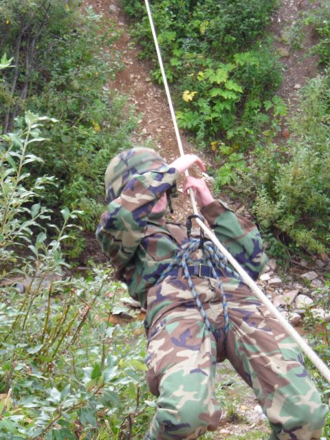 2003 Jeep TJ - A person in military camouflage rappels down a steep, vegetated incline using a rope and harness.