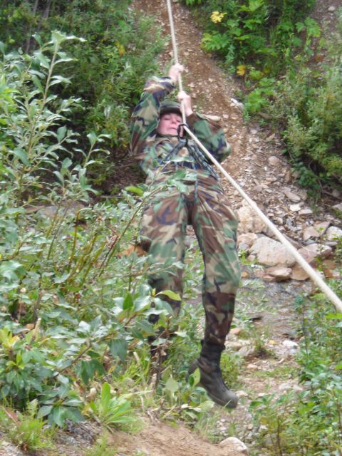 2003 Jeep TJ - A person in camouflage gear rappels down a steep, vegetated slope using a rope.