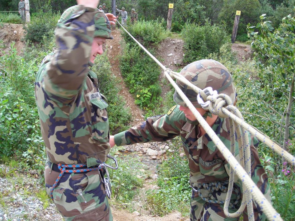 Soldiers in camouflage uniforms practice with ropes and harnesses outdoors