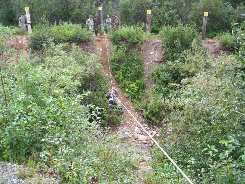 Soldiers rappelling down a slope during a training exercise. Some soldiers stand at the top of the slope