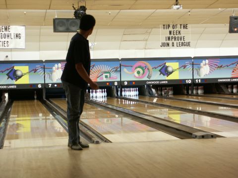 2001 Mercury Grand Marquis - A person stands on a bowling lane, ready to roll the ball. The alley features multiple lanes and overhead score displays.