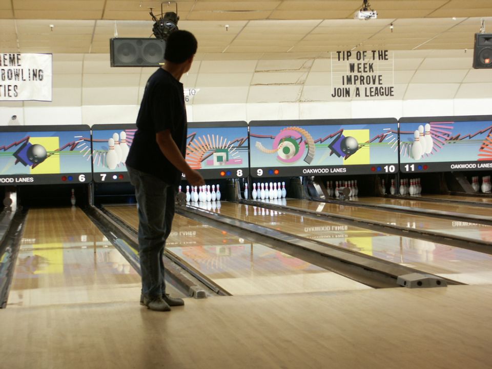 Bowling alley with lanes, pins, and a person preparing to bowl. Signage visible