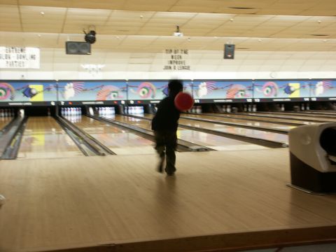 2001 Mercury Grand Marquis - A person bowls a red ball down a lane in a bowling alley.
