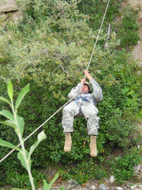 2003 Jeep TJ - A soldier is rappelling down a rocky, vegetated slope using a rope and harness.