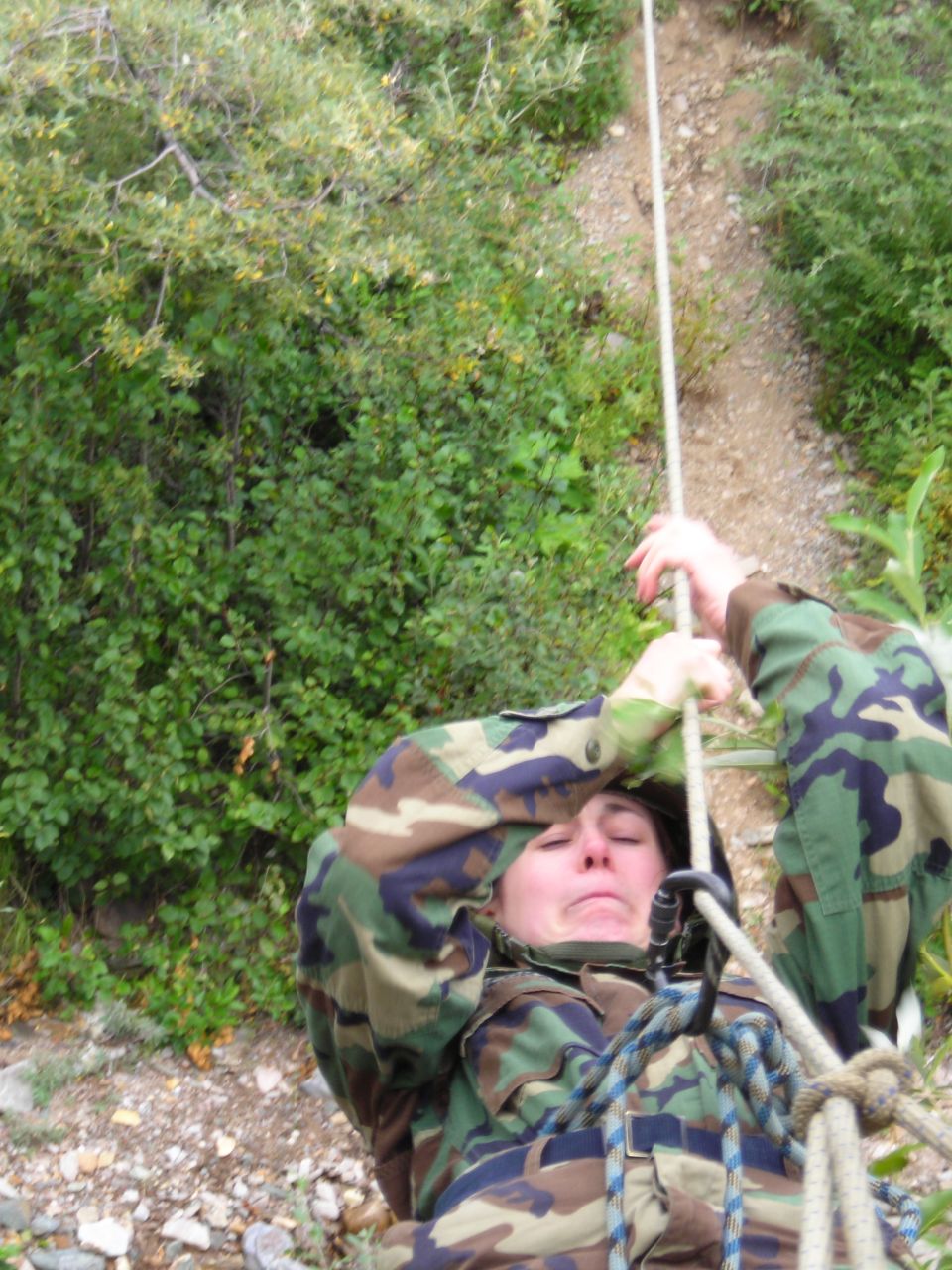 Person in camouflage rappelling down a rocky slope