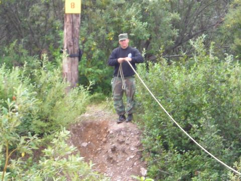 2003 Jeep TJ - A man stands on a dirt mound, holding a rope, with dense foliage in the background.