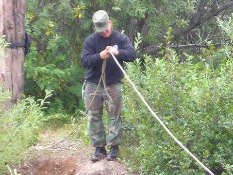 2003 Jeep TJ - A person wearing camouflage pants and a dark sweatshirt is tying a rope in an outdoor setting with dense foliage.