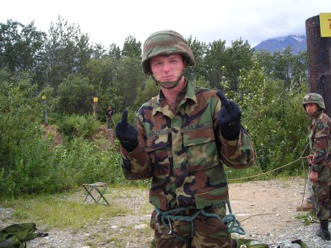 2003 Jeep TJ - Two soldiers in camouflage uniforms are in an outdoor training area with trees and mountains in the background.