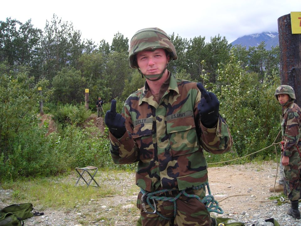 Soldier in camouflage uniform with helmet gives the finger. Another soldier stands in the background