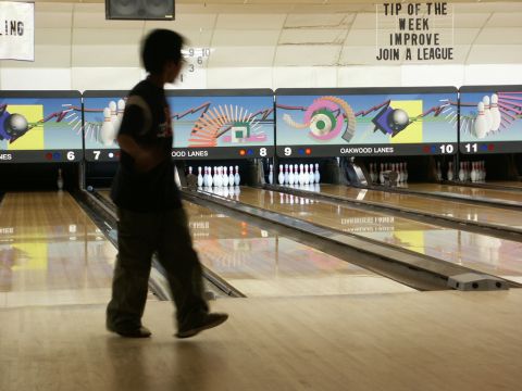 2001 Mercury Grand Marquis - A person walks past bowling lanes in a bowling alley, with pins set up and lane graphics displayed.