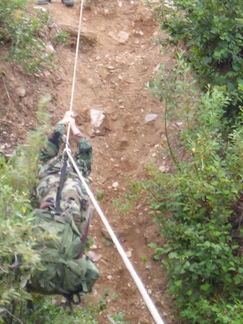 2003 Jeep TJ - A person in camouflage gear rappels down a steep, rocky incline surrounded by vegetation.