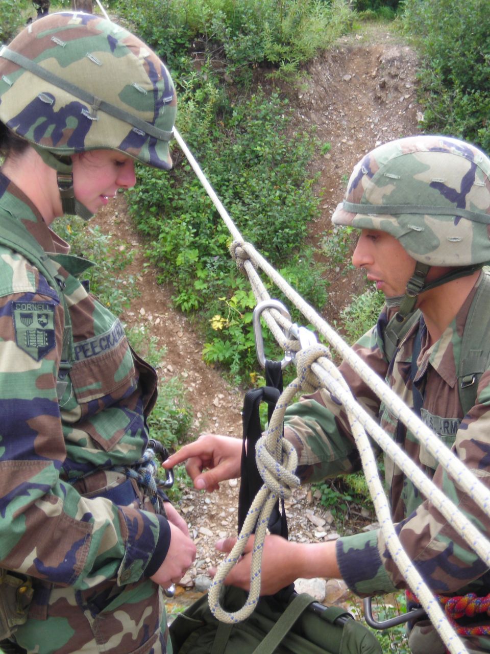 Two soldiers in camouflage uniforms practicing rappelling with ropes and carabiners
