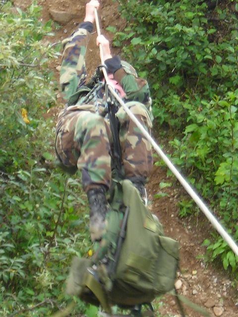 2003 Jeep TJ - Soldier in camouflage gear rappels down a steep, wooded incline using a rope.