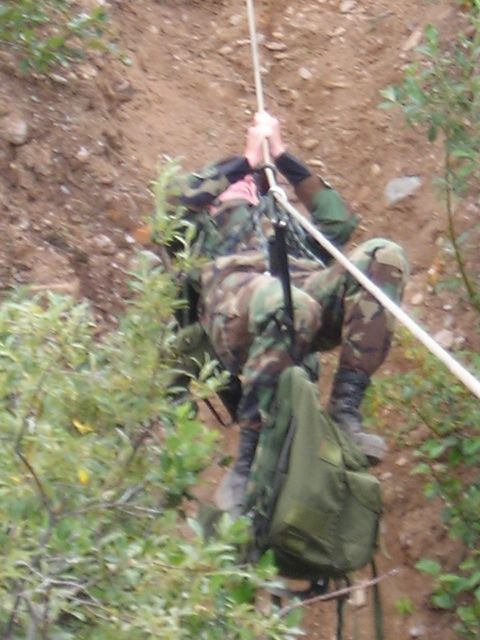 2003 Jeep TJ - A person is rappelling down a steep, dirt-covered slope with vegetation on the sides.
