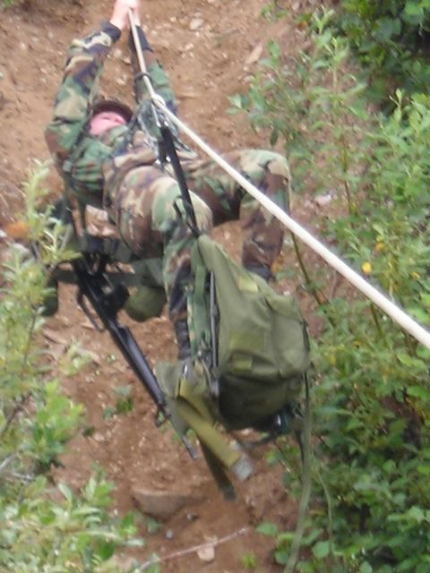 2003 Jeep TJ - A soldier in camouflage gear descends a steep, wooded incline using a rope and harness system.