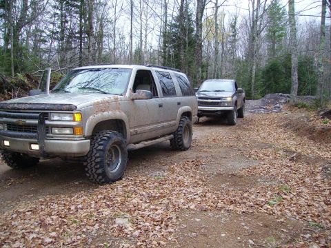 2000 Chevrolet Tahoe - A dirty Chevrolet Tahoe and a pickup truck are parked on a wooded dirt road.