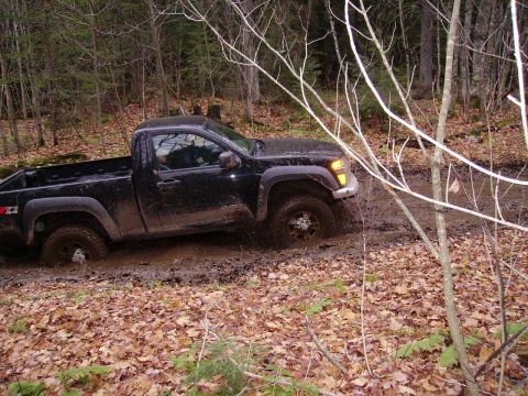 2000 Chevrolet Tahoe - A black pickup truck navigates a muddy trail through a wooded area, with its tires deep in the mire.