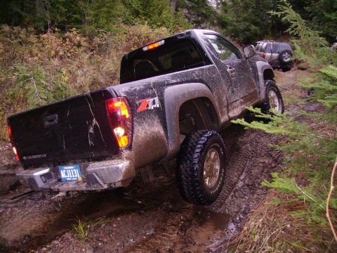 2000 Chevrolet Tahoe - A black Chevrolet Colorado Z71 navigates a challenging muddy off-road trail, with another SUV following behind.