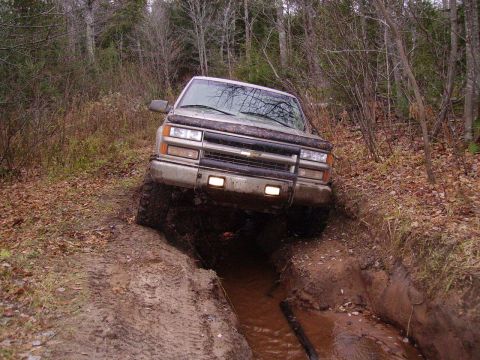 2000 Chevrolet Tahoe - This Chevrolet pickup truck is shown driving through a muddy off-road trail with trees in the background.