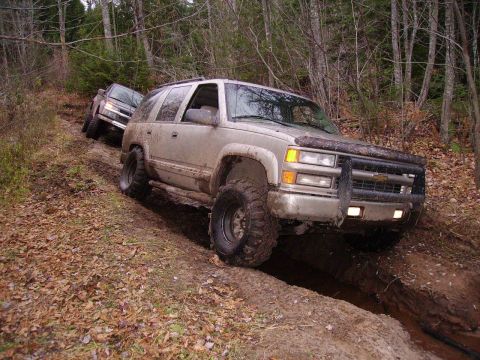 2000 Chevrolet Tahoe - Two SUVs navigate a muddy, wooded trail with fallen leaves on the ground.