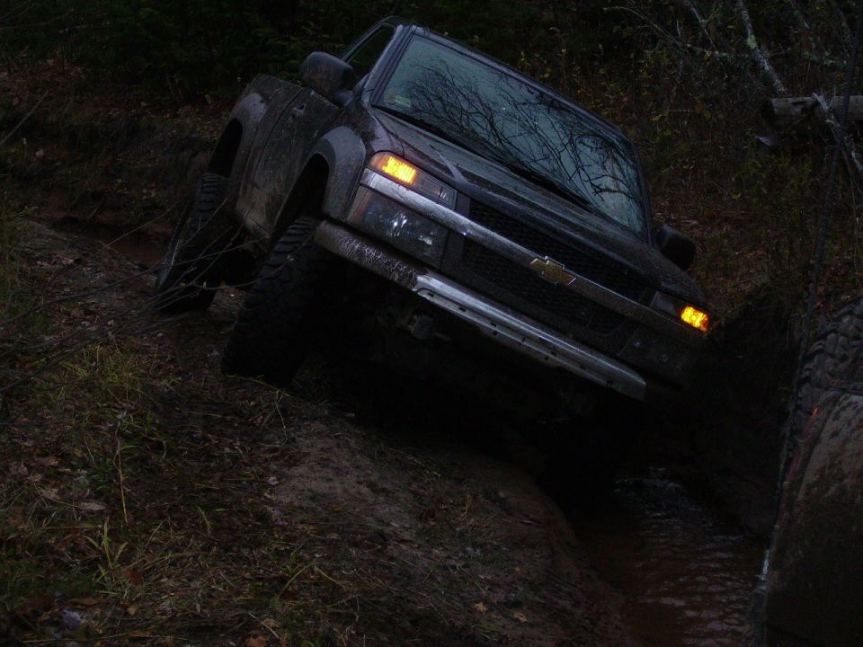 Dark pickup truck with a chrome grille and orange turn signals, tilted on a muddy incline
