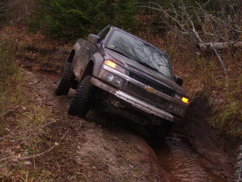 2000 Chevrolet Tahoe - This dark pickup truck is shown navigating a challenging muddy off-road trail, demonstrating its off-road capabilities.