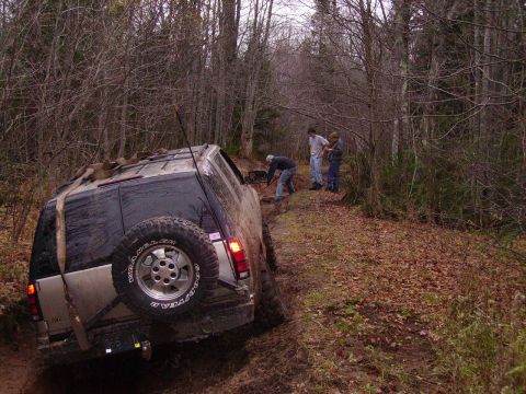 2000 Chevrolet Tahoe - An SUV is stuck in the mud on a wooded trail while people attempt to free it.