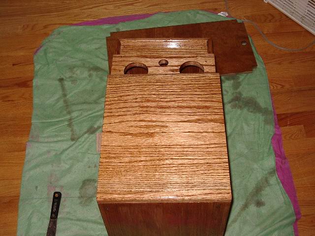 Wooden center console part with two circular cutouts and a smaller central hole, resting on a green cloth on a wooden floor