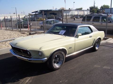 2002 Ford Mustang - A classic Mustang is parked in a lot with a fence and buildings in the background.