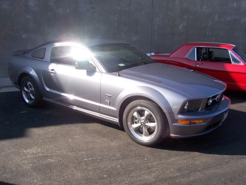 2002 Ford Mustang - A silver Ford Mustang GT is parked in front of a red classic car, with a Supermotors.net logo visible at the bottom right.