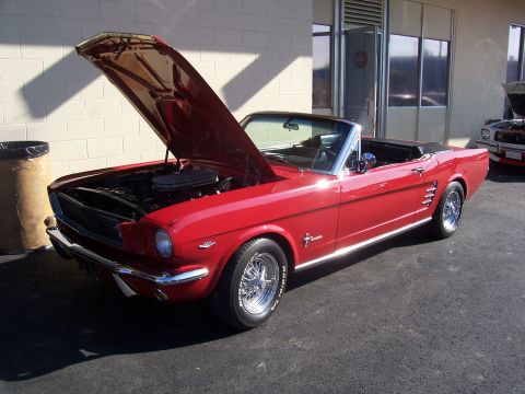 2002 Ford Mustang - A classic red convertible is displayed with its hood up, parked next to a building.
