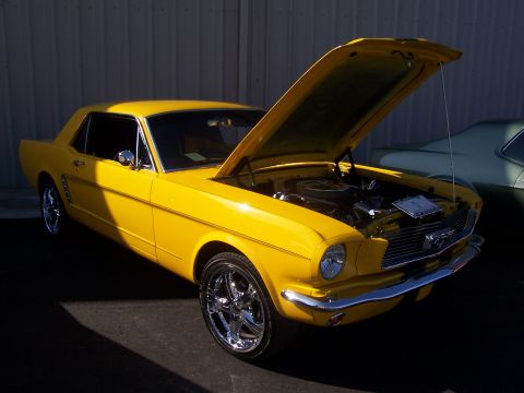 2002 Ford Mustang - A yellow 1965 Ford Mustang coupe is displayed with its hood open, parked next to another vehicle.