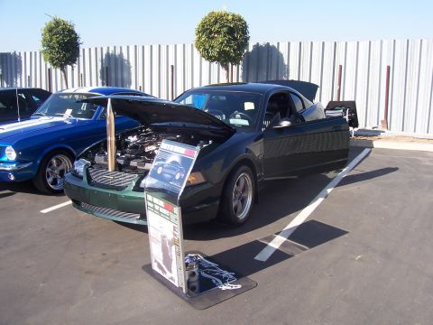 2002 Ford Mustang - A dark green Ford Mustang is displayed with its hood and door open, parked beside a blue classic Mustang.