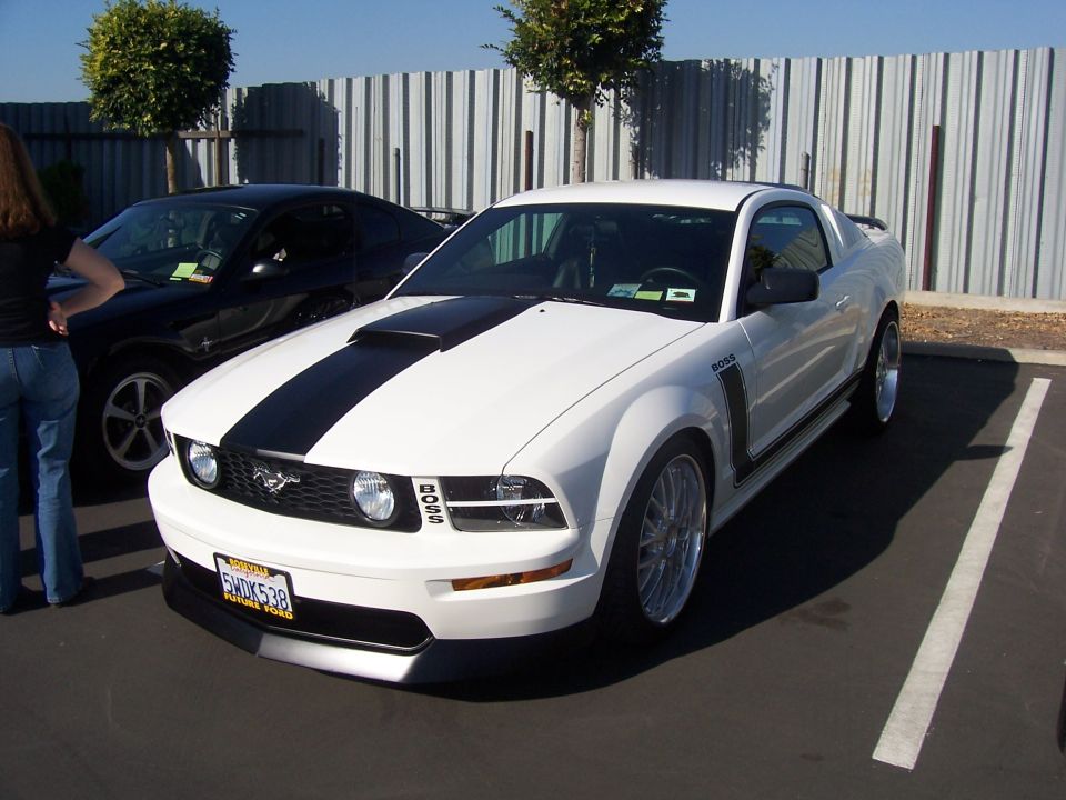 White Ford Mustang Boss 302 with black stripes and custom wheels, parked in a lot