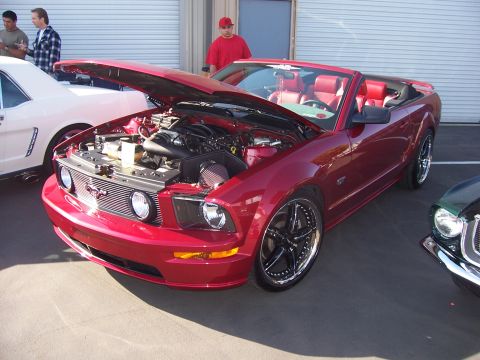 2002 Ford Mustang - A red convertible Mustang is displayed with its hood open, revealing the engine bay. Another vehicle is parked nearby.