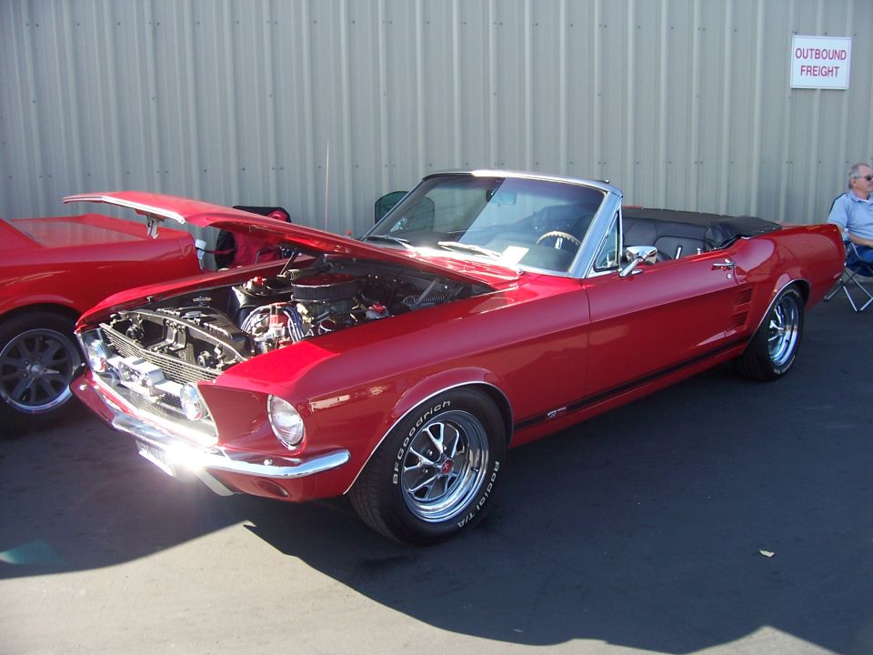 Red 1960s Mustang convertible, top down and hood up over a V8, at a show