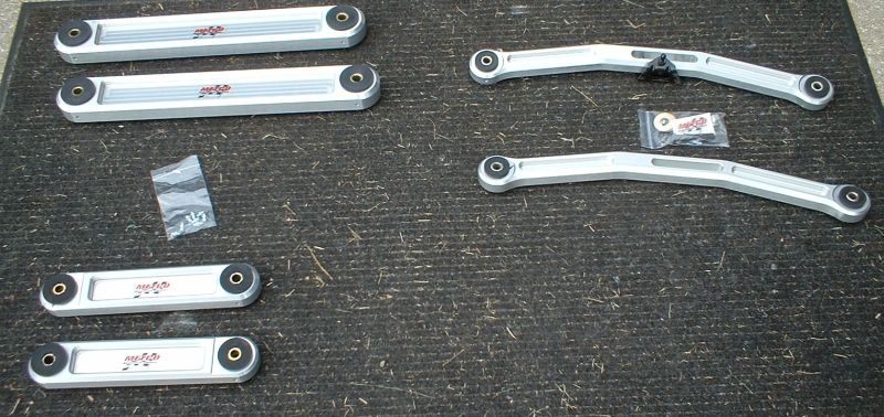 Set of polished aluminum suspension control arms laid out on carpet