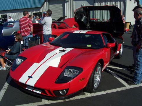 2002 Ford Mustang - A red 2005-2006 Ford GT with white racing stripes is displayed with its doors open at an outdoor event.