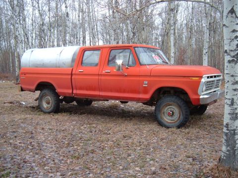 1979 Ford Bronco - This four-door pickup truck features a custom tank bed and is parked outdoors among trees.