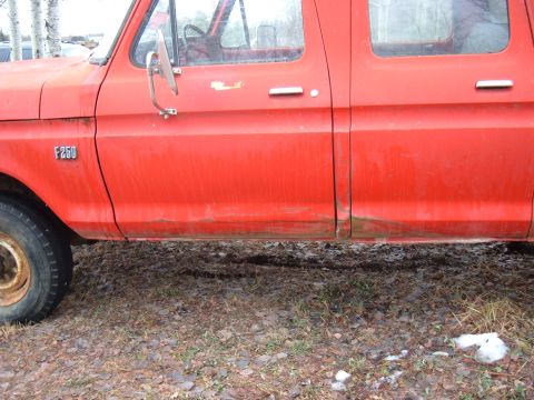 1979 Ford Bronco - This red Ford F-250 truck shows significant rust on its lower body panels and a partial view of the front wheel.