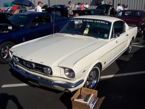 2002 Ford Mustang - A classic white Ford Mustang is displayed at an outdoor car event with other vehicles and people around.
