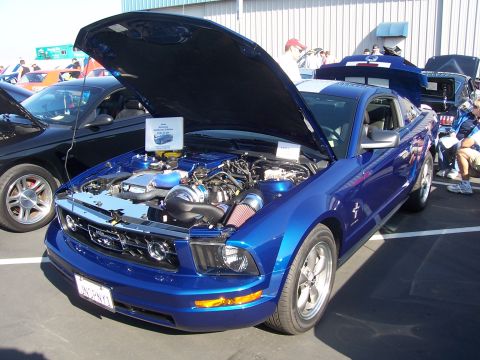 2002 Ford Mustang - A blue 2005 Ford Mustang is displayed with its hood open, revealing engine modifications at a car show.