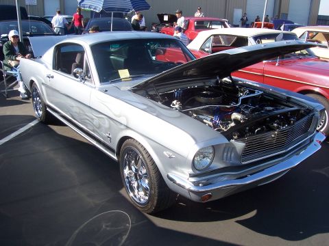 2002 Ford Mustang - A classic silver Mustang with custom flame paint is displayed with its hood open at an outdoor car show.