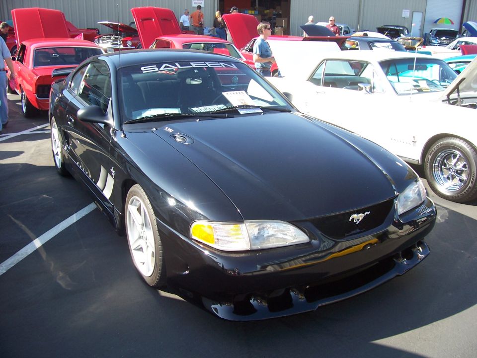 Black Saleen Mustang with "SALEEN" banner on windshield, parked at an outdoor car show