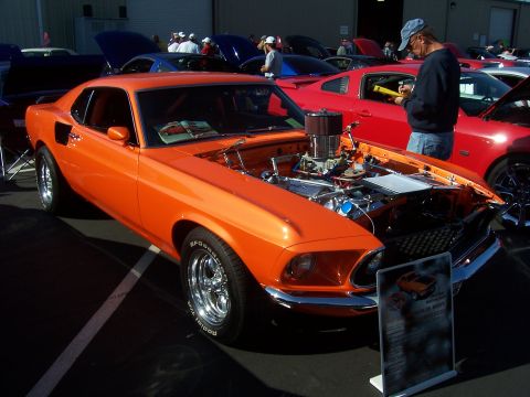 2002 Ford Mustang - This orange 1969 Mustang fastback features chrome wheels and an open hood revealing its engine, displayed at a car show.