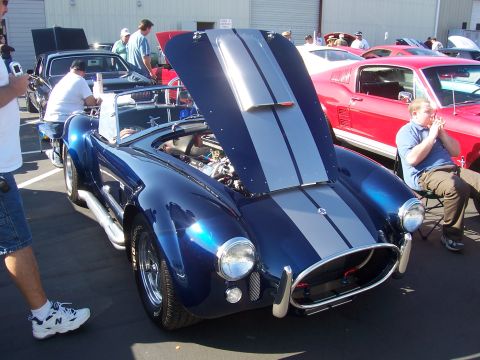 2002 Ford Mustang - A blue Cobra car with its hood open is displayed at an outdoor car show, with other vehicles in the background.
