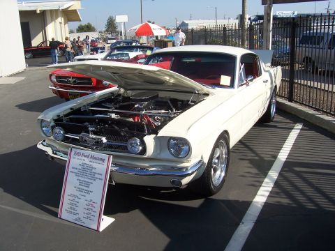 2002 Ford Mustang - A white 1965 Ford Mustang is displayed with its hood open, showing the engine. Another Mustang is parked nearby.