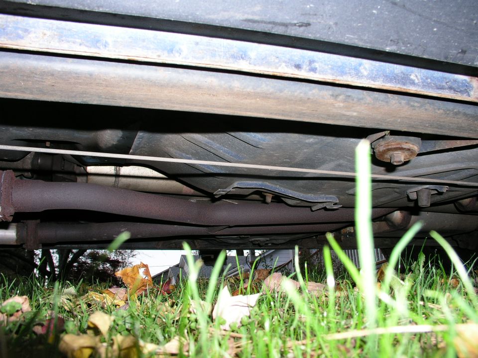 Underside view of a vehicle frame rail, driveshaft and exhaust over grass