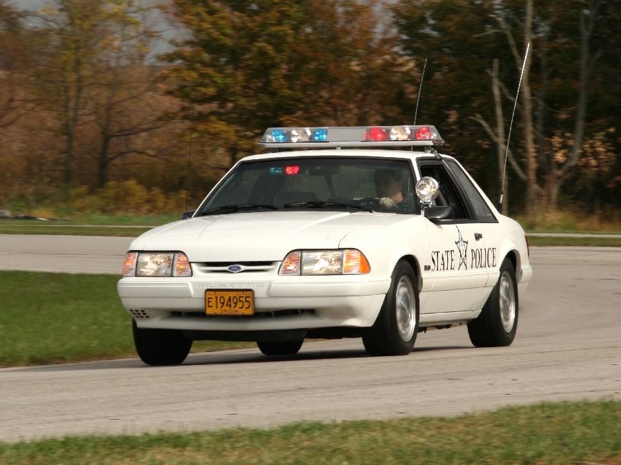 White Fox-body Mustang state police car with roof lightbar cornering on a racetrack